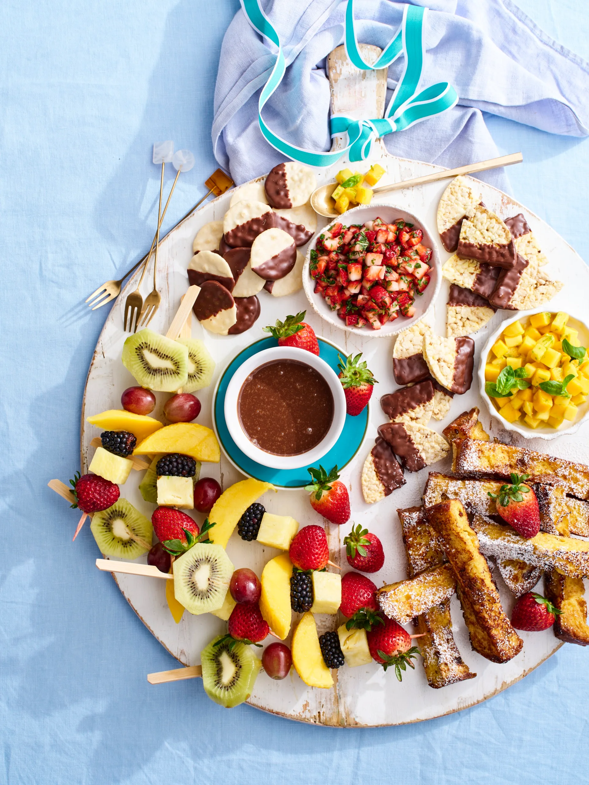 christmas dessert board on round wooden board with skewers of fruit, french toast and strawberry salsa