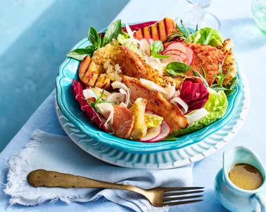 brightly coloured peach and ham salad with fresh salad ingredients on blue table in teal plate