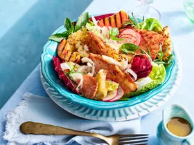 brightly coloured peach and ham salad with fresh salad ingredients on blue table in teal plate