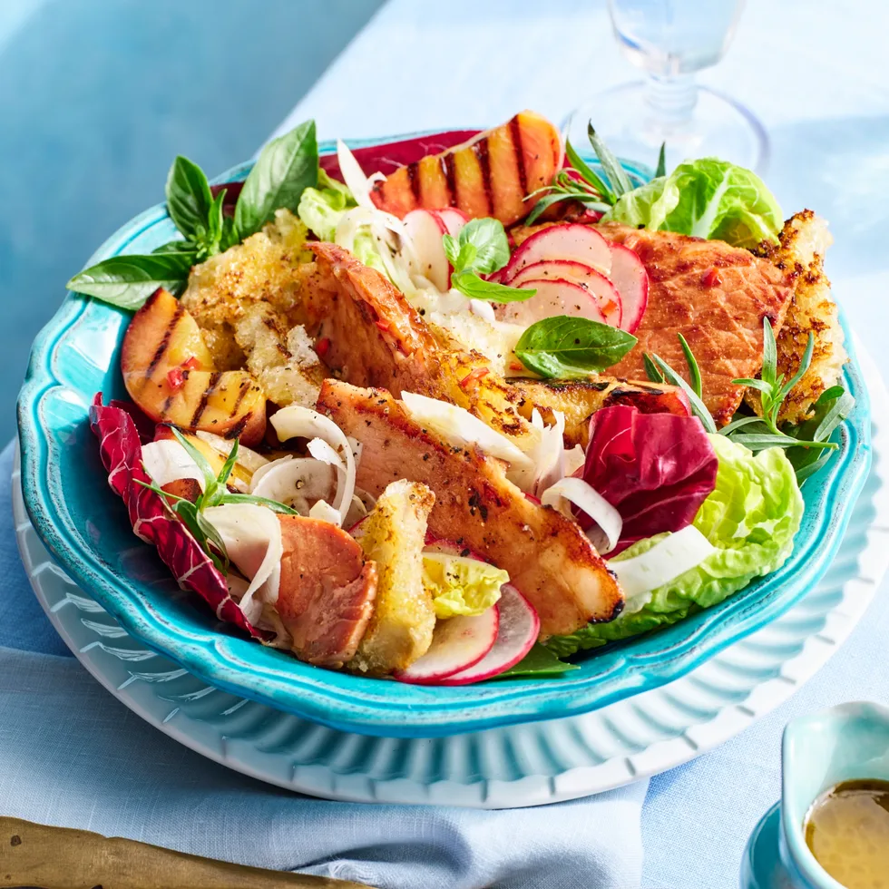brightly coloured peach and ham salad with fresh salad ingredients on blue table in teal plate