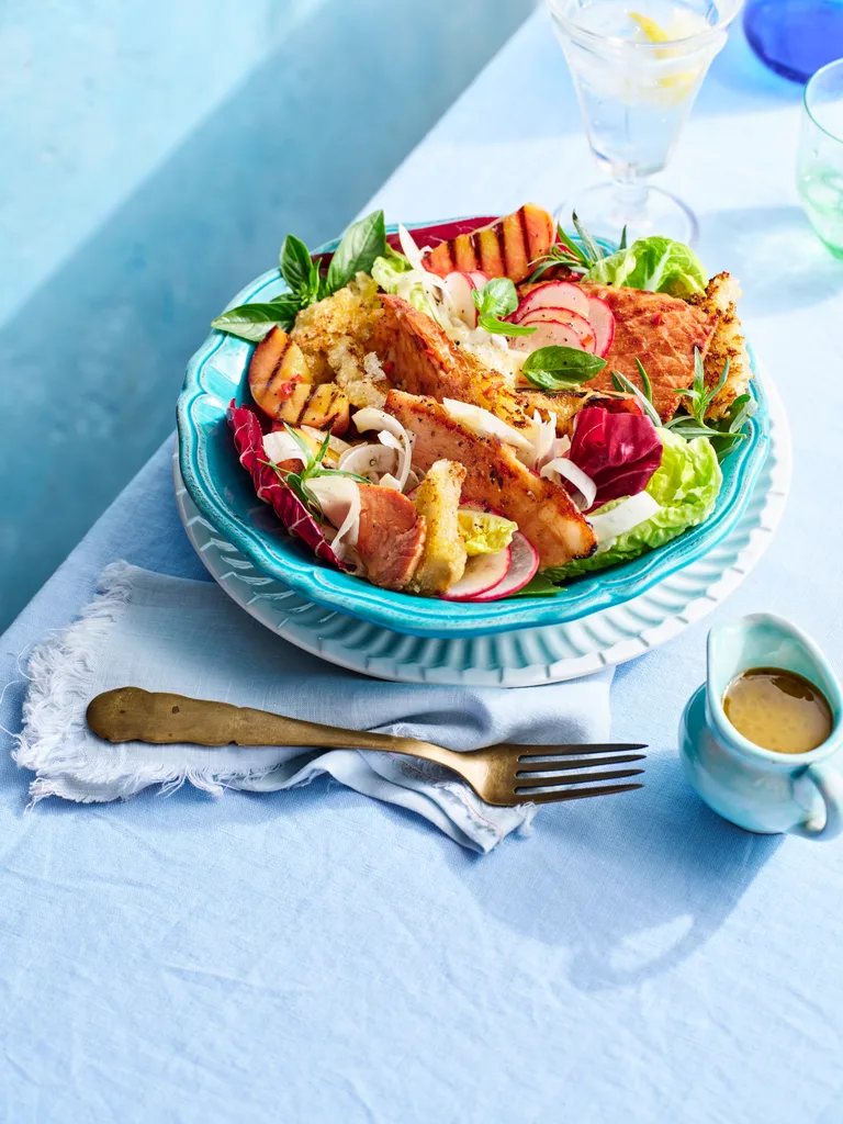 brightly coloured peach and ham salad with fresh salad ingredients on blue table in teal plate