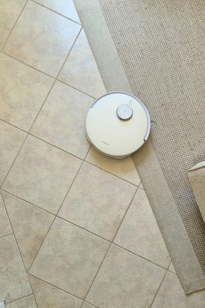 White robot vacuum. cleaner and mop by Ecovacs Deebot cleaning tiled and carpeted floor