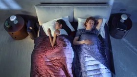 A couple sleeping under the Eight Sleep Pod smart mattress cover, showing dual temperature zones—one warm red and one cool blue—demonstrating personalised sleep temperature control. Featured in a Better Homes & Gardens Australia Eight Sleep review ahead of Black Friday sales