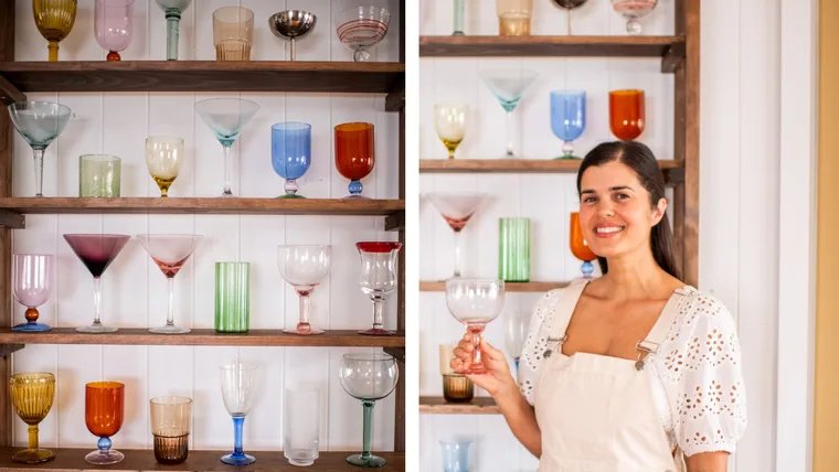 geneva vanderzeil standing in front of glasses holding coloured yellow glass with shelving unit on the left showing glassware