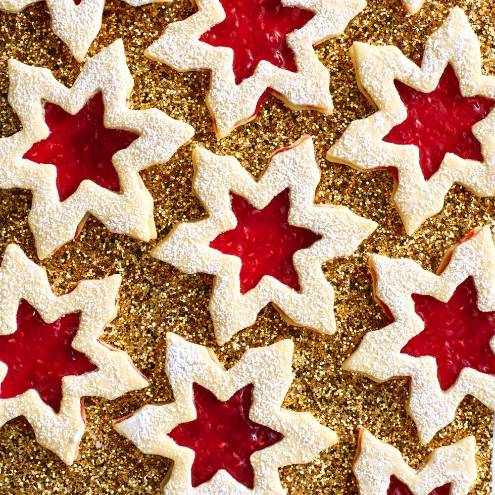 linzer biscuit in snowflake shapes on gold glittery table with jam in the middle