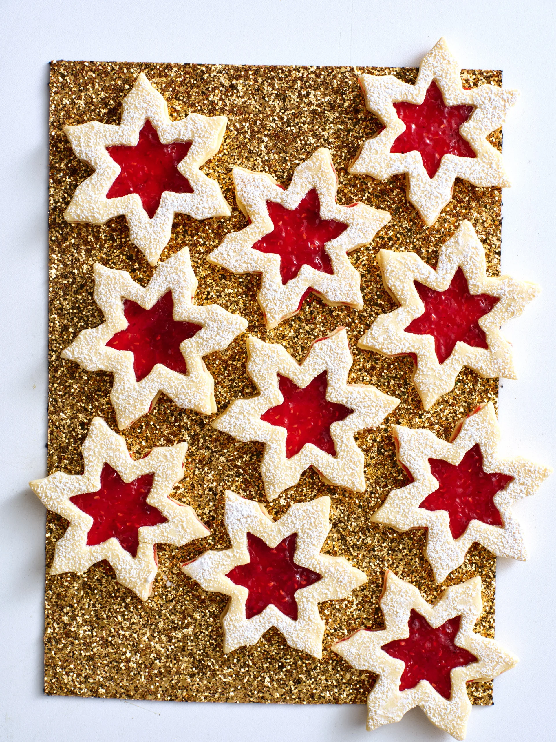 linzer biscuit in snowflake shapes on gold glittery table with jam in the middle