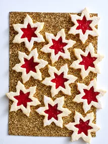 linzer biscuit in snowflake shapes on gold glittery table with jam in the middle