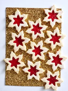 linzer biscuit in snowflake shapes on gold glittery table with jam in the middle