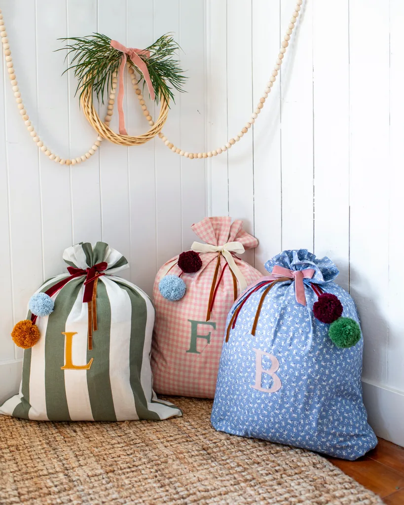 three personalised santa sacks with poms poms and ribbon and letters embroidered into front of sack