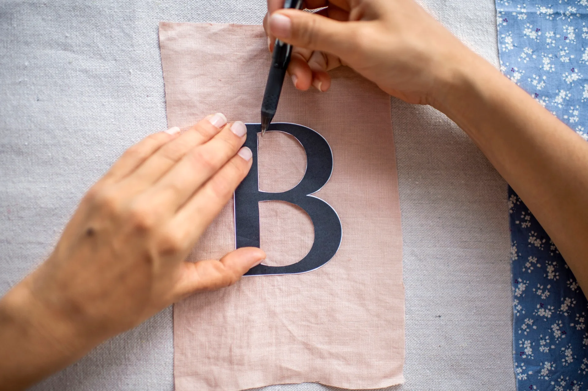 mãos traçando a letra 'b' em uma amostra de tecido