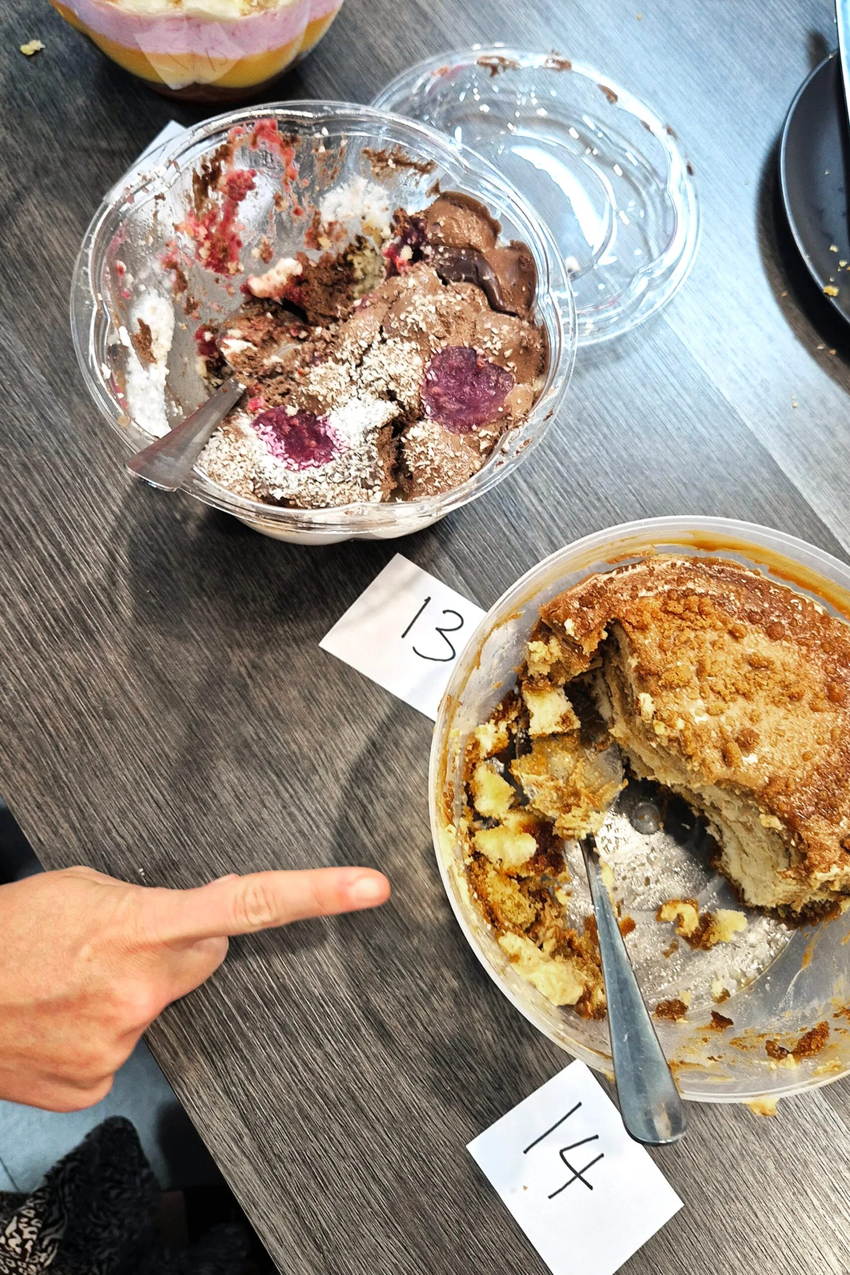 Two bowls of supermarket trifles on a table. A hand is pointing at one of the trifles.