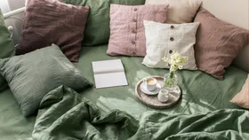A top-down image of a bed with linen throw cushions scattered on top of a green linen sheet