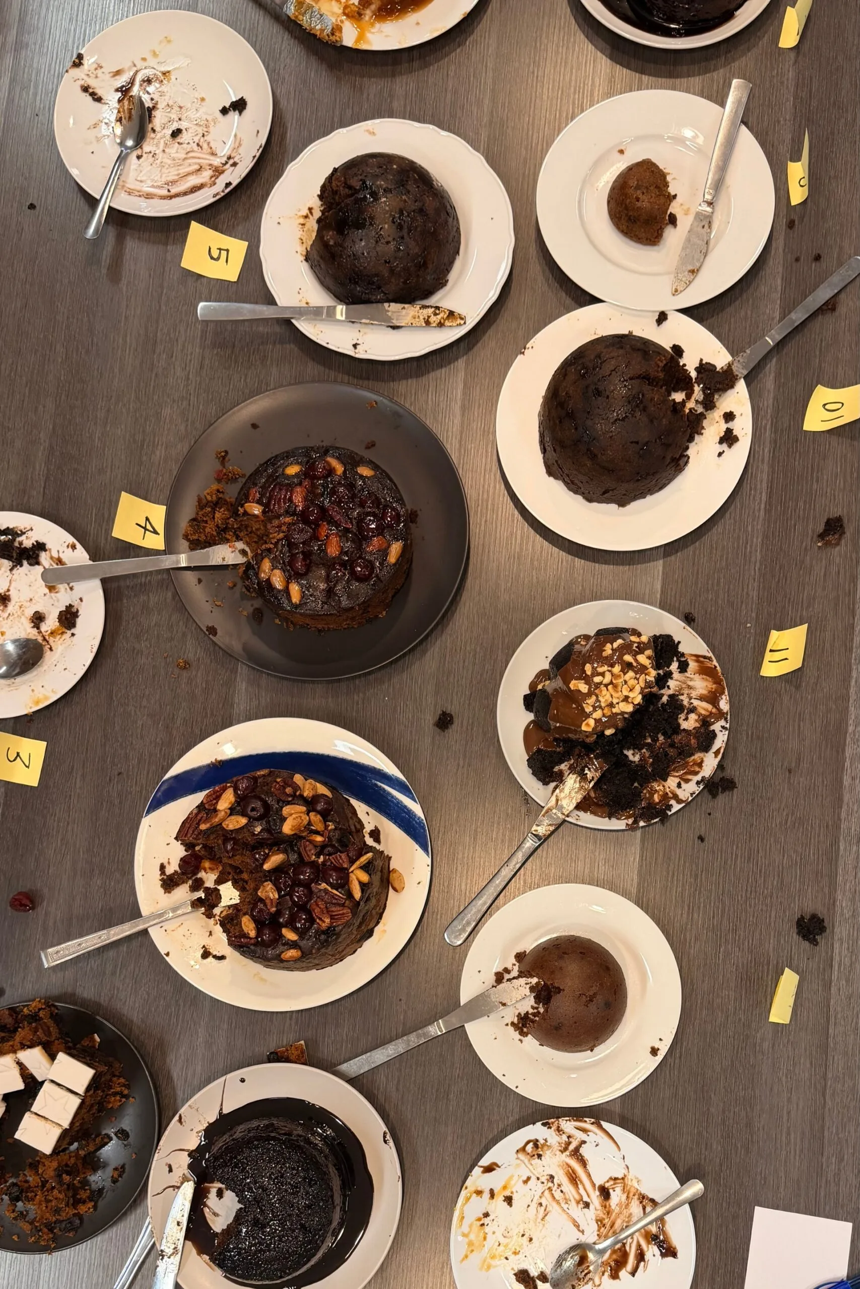 christmas puddings on plates with knives cut into them and firty empty plates surrounding them