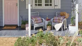Cottage painted in pink and purple with two wicker armchairs on the verandah.
