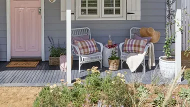 Cottage painted in pink and purple with two wicker armchairs on the verandah.