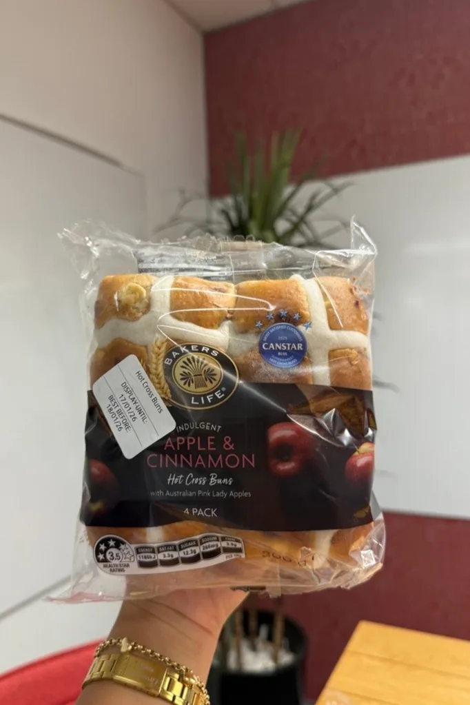apple and cinnamon hot cross buns held up in front of camera with wooden table behind