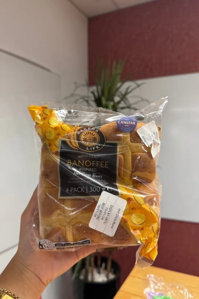 banoffee hot cross buns held up in front of camera with wooden table behind