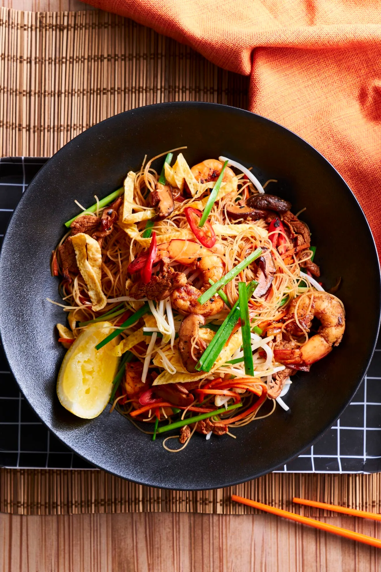 singapore noodles in black bowl with slice of lemon the side
