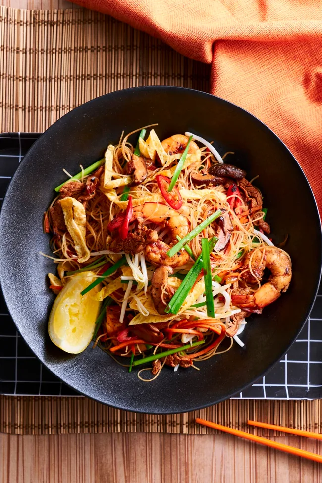 singapore noodles in black bowl with slice of lemon the side