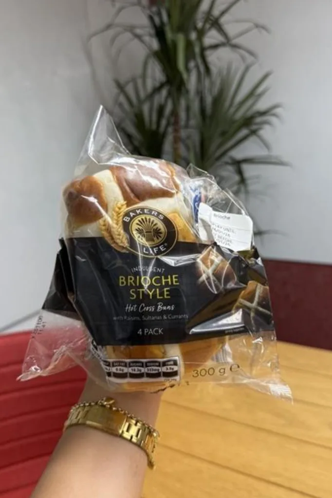 brioche style hot cross buns held up in front of camera with wooden table behind