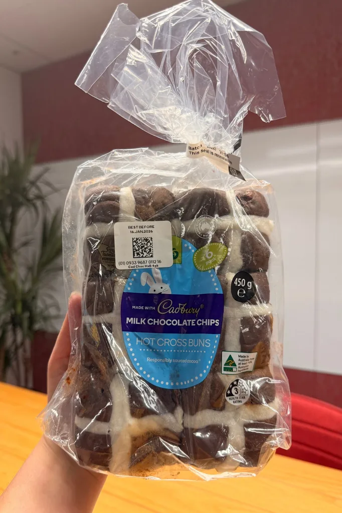 cadbury milk chocolate hot cross buns held up in front of camera with wooden table behind