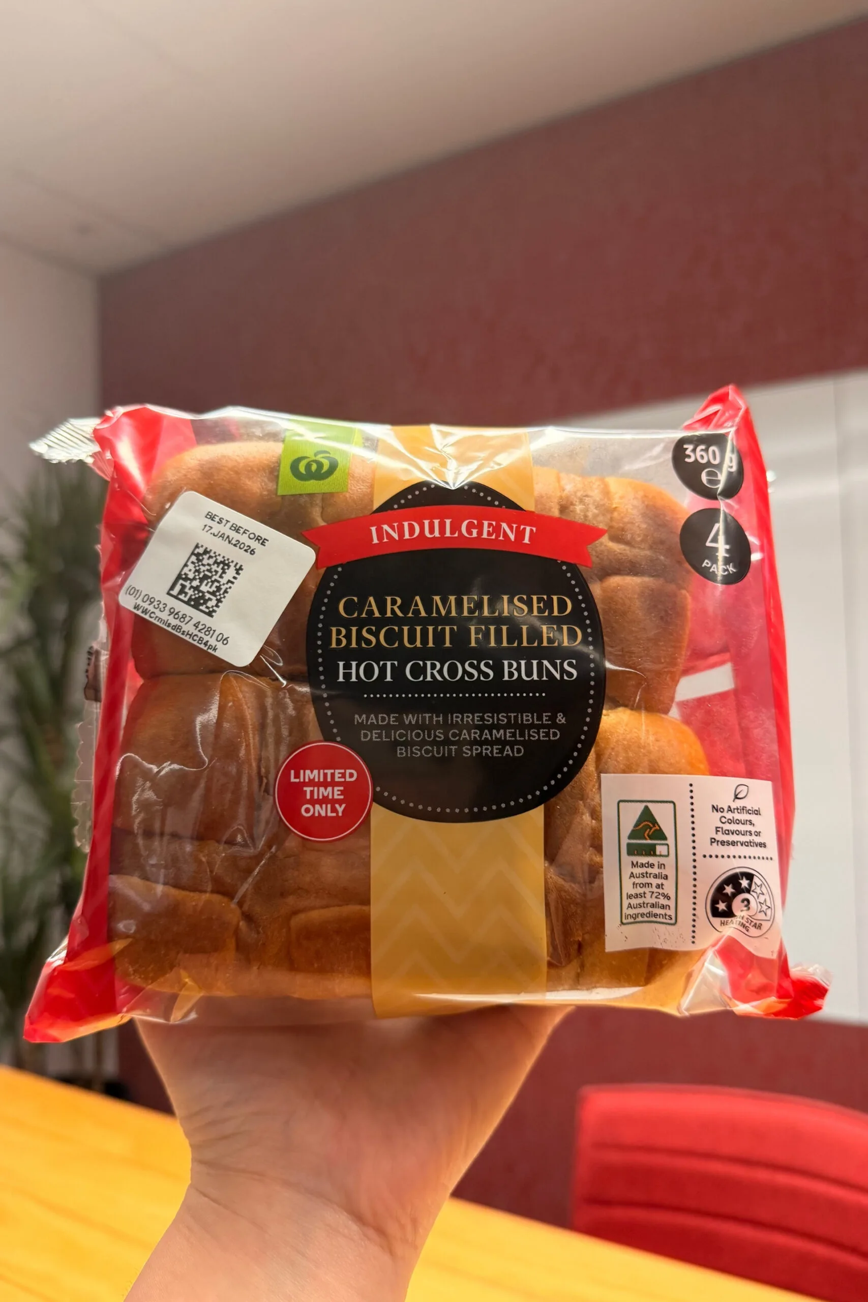 caramelised biscuit filled hot cross buns held up in front of camera with wooden table behind