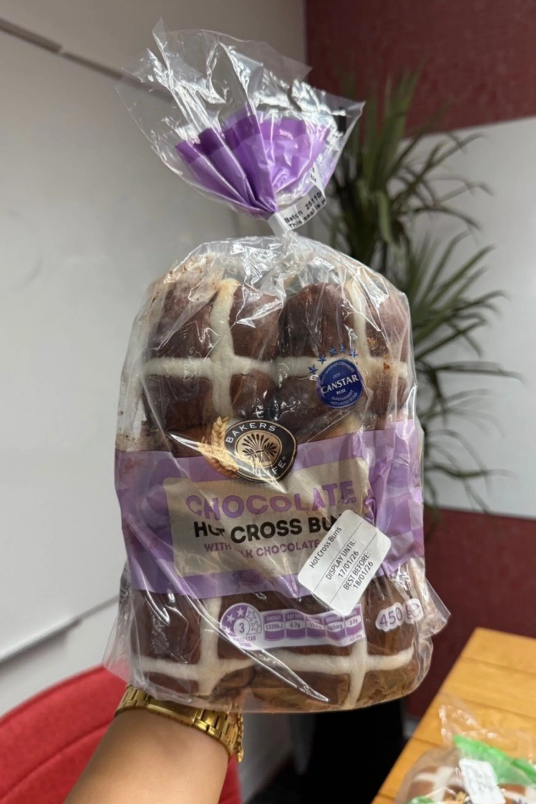 chocolate hot cross buns held up in front of camera with wooden table behind