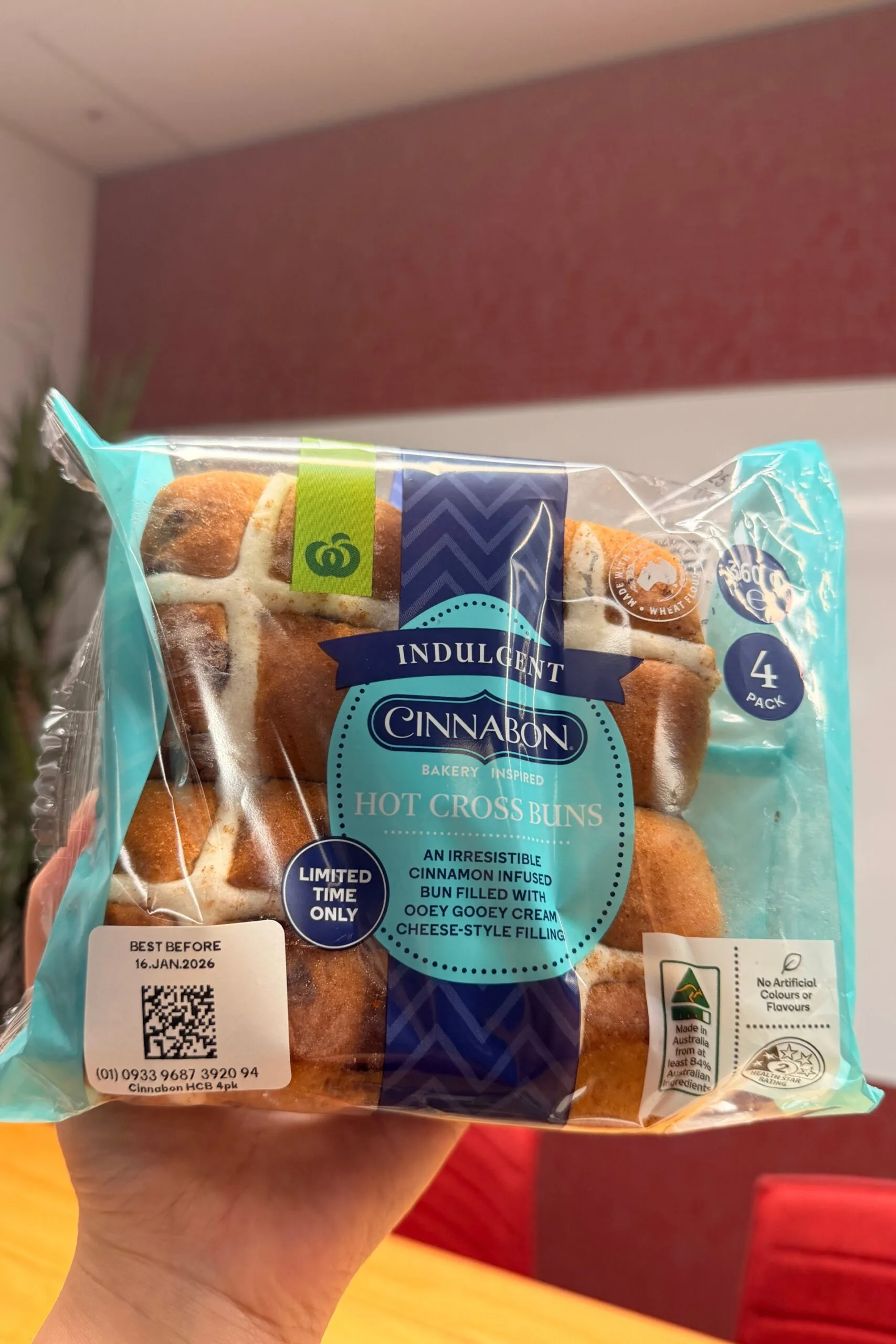 cinnabon hot cross buns held up in front of camera with wooden table behind