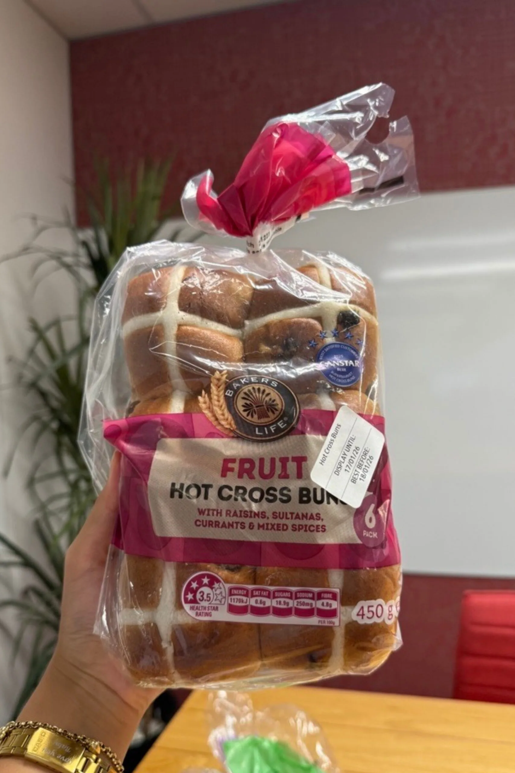 fruit hot cross buns held up in front of camera with wooden table behind