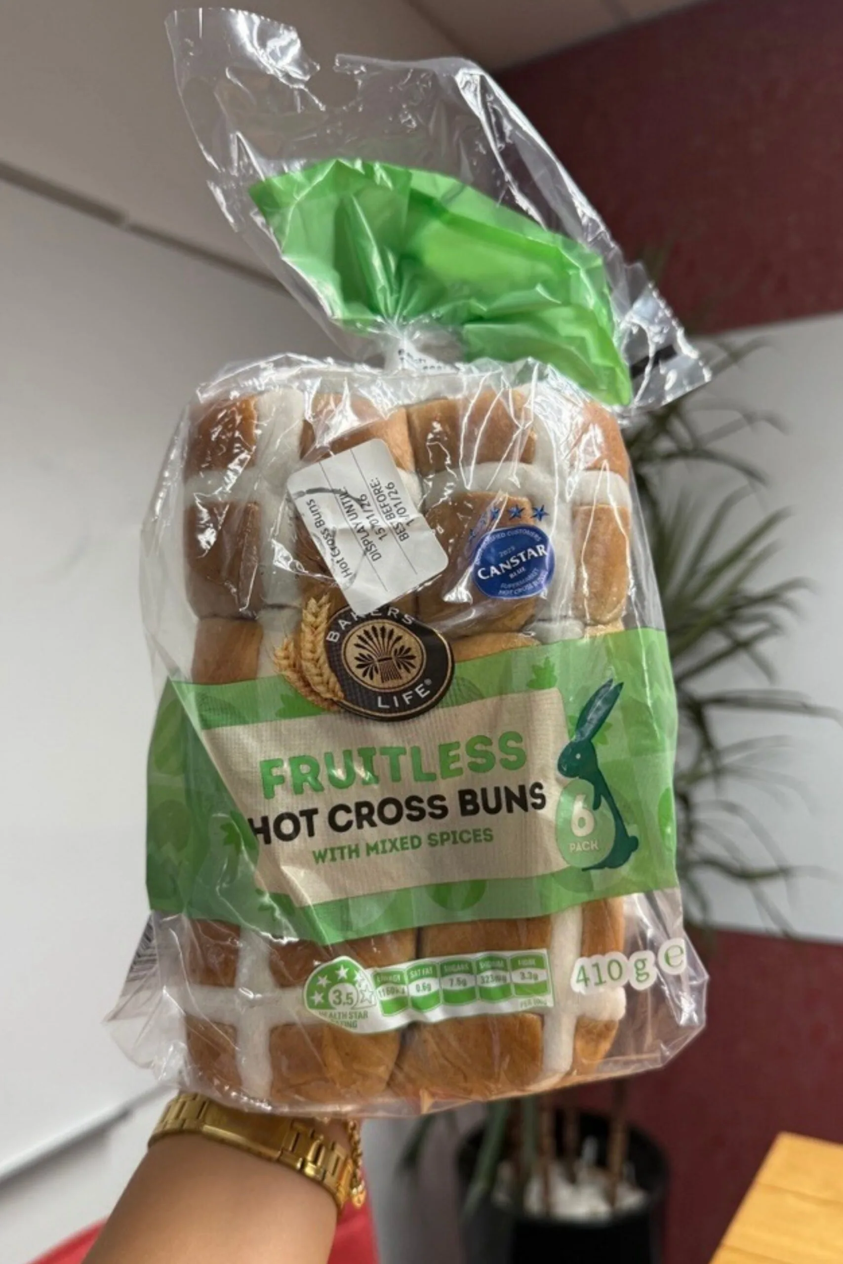 fruitless hot cross buns held up in front of camera with wooden table behind