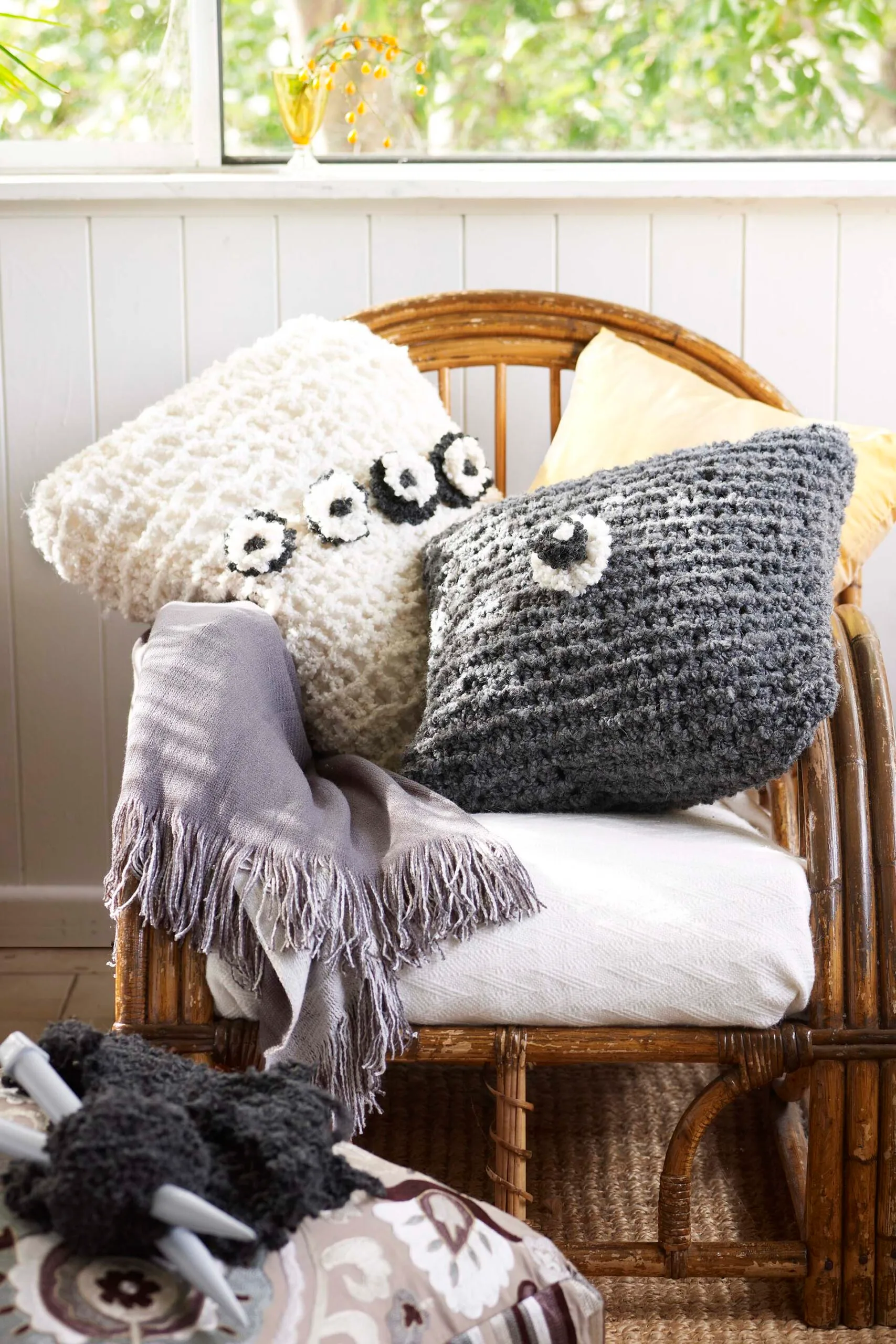 Knitted throw and cushion covers with knitting needles in foreground