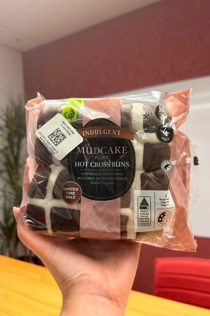 mudcake hot cross buns held up in front of camera with wooden table behind