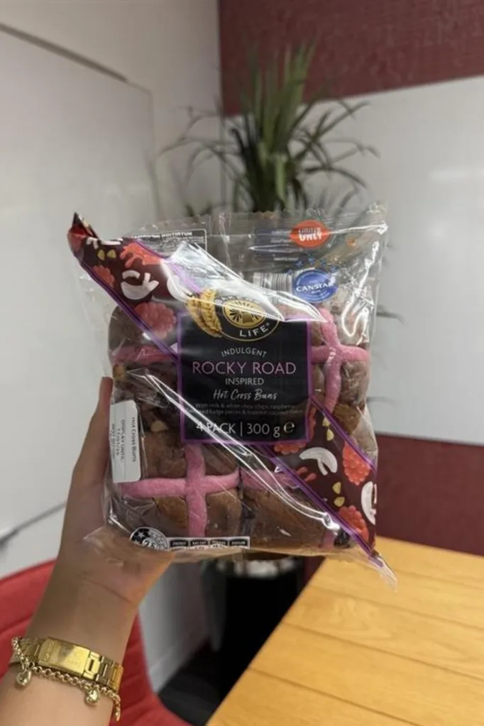 rocky road hot cross buns held up in front of camera with wooden table behind