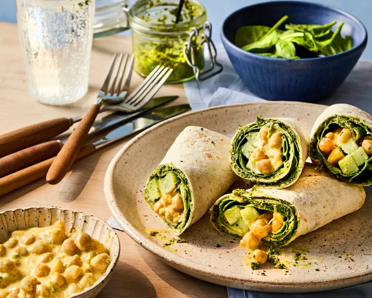 cross section of chickpea vegan wrap piled up on plate and glass of lemonade behind it.