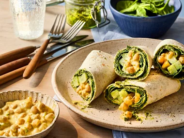 cross section of chickpea vegan wrap piled up on plate and glass of lemonade behind it.