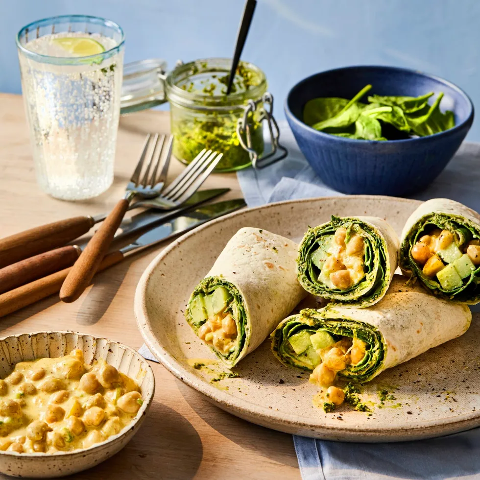 cross section of chickpea vegan wrap piled up on plate and glass of lemonade behind it.
