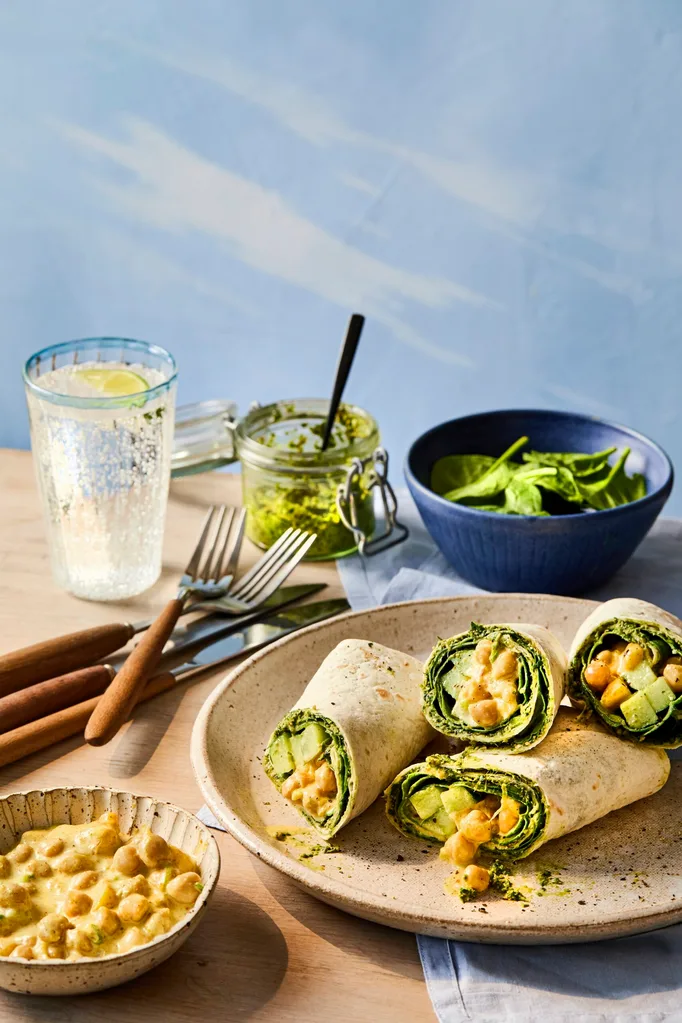cross section of chickpea vegan wrap piled up on plate and glass of lemonade behind it.