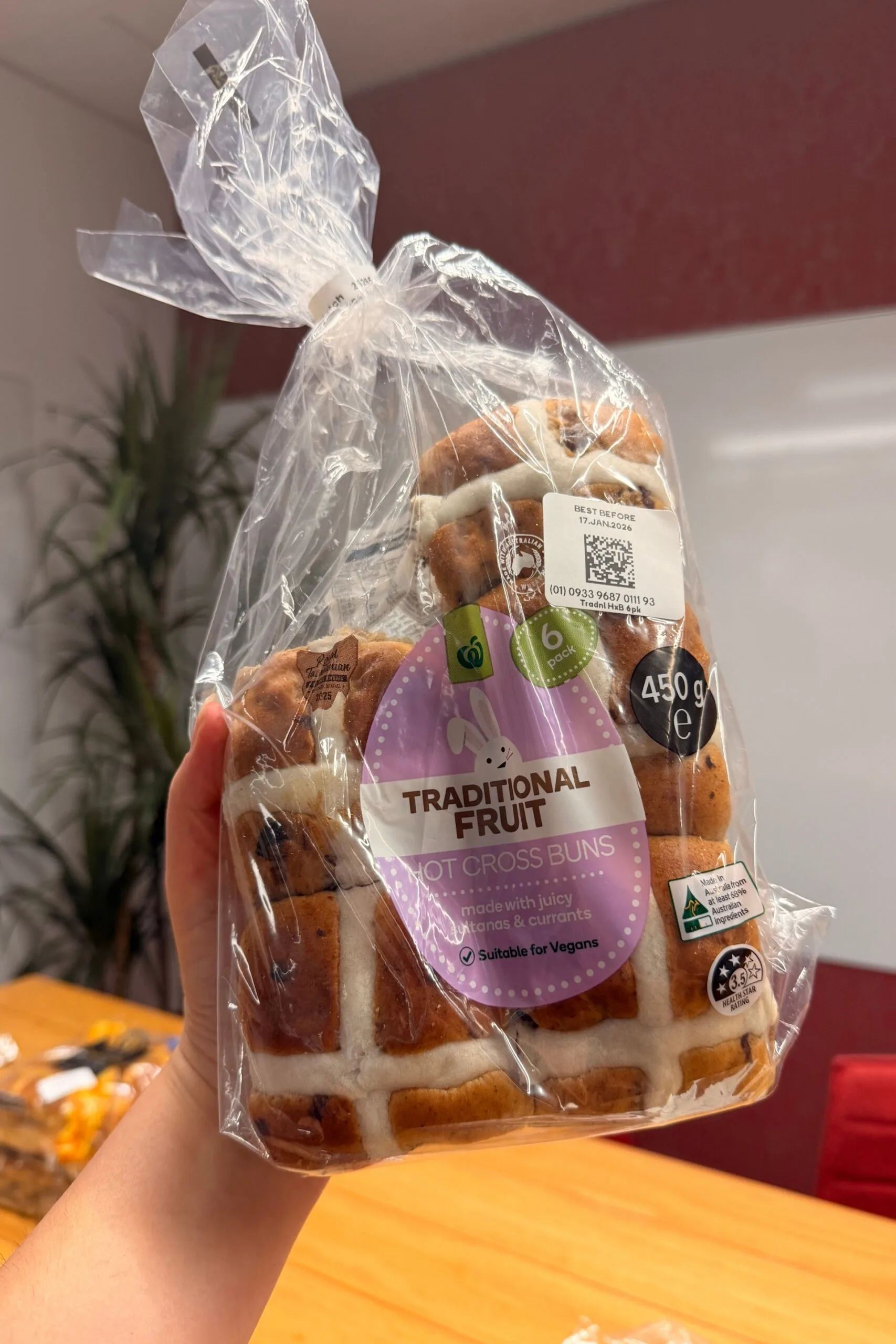 traditional fruit hot cross buns held up in front of camera with wooden table behind with one missing