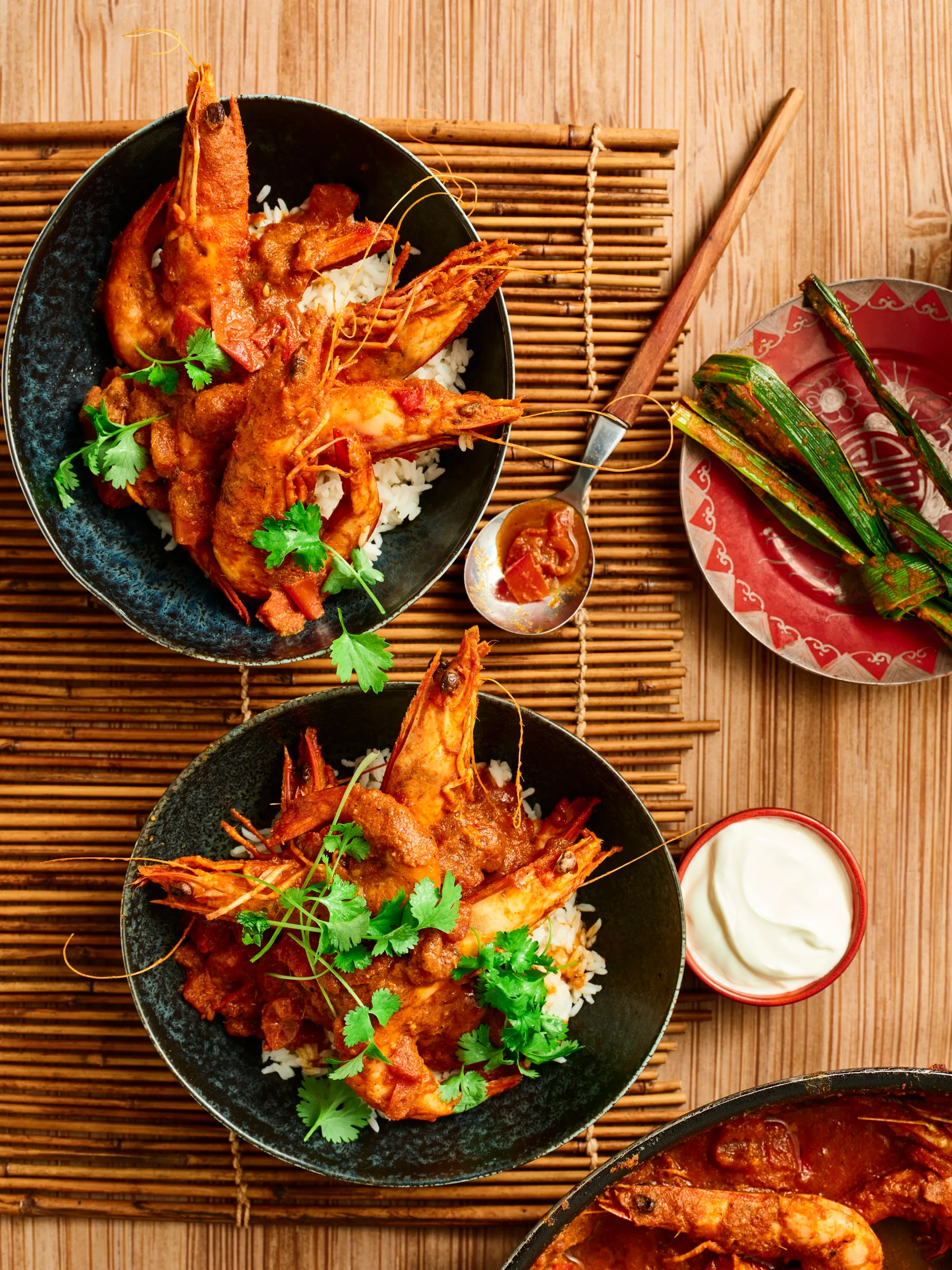 tomato and prawn curry with crunchy prawns with head still on herbs on top in a black bowl