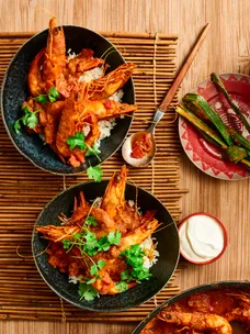 tomato and prawn curry with crunchy prawns with head still on herbs on top in a black bowl