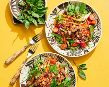 thai beef salad with beef and coriander on top of leafy green salad with mint and coriander on separate plate on the side