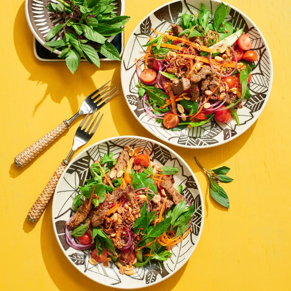 thai beef salad with beef and coriander on top of leafy green salad with mint and coriander on separate plate on the side