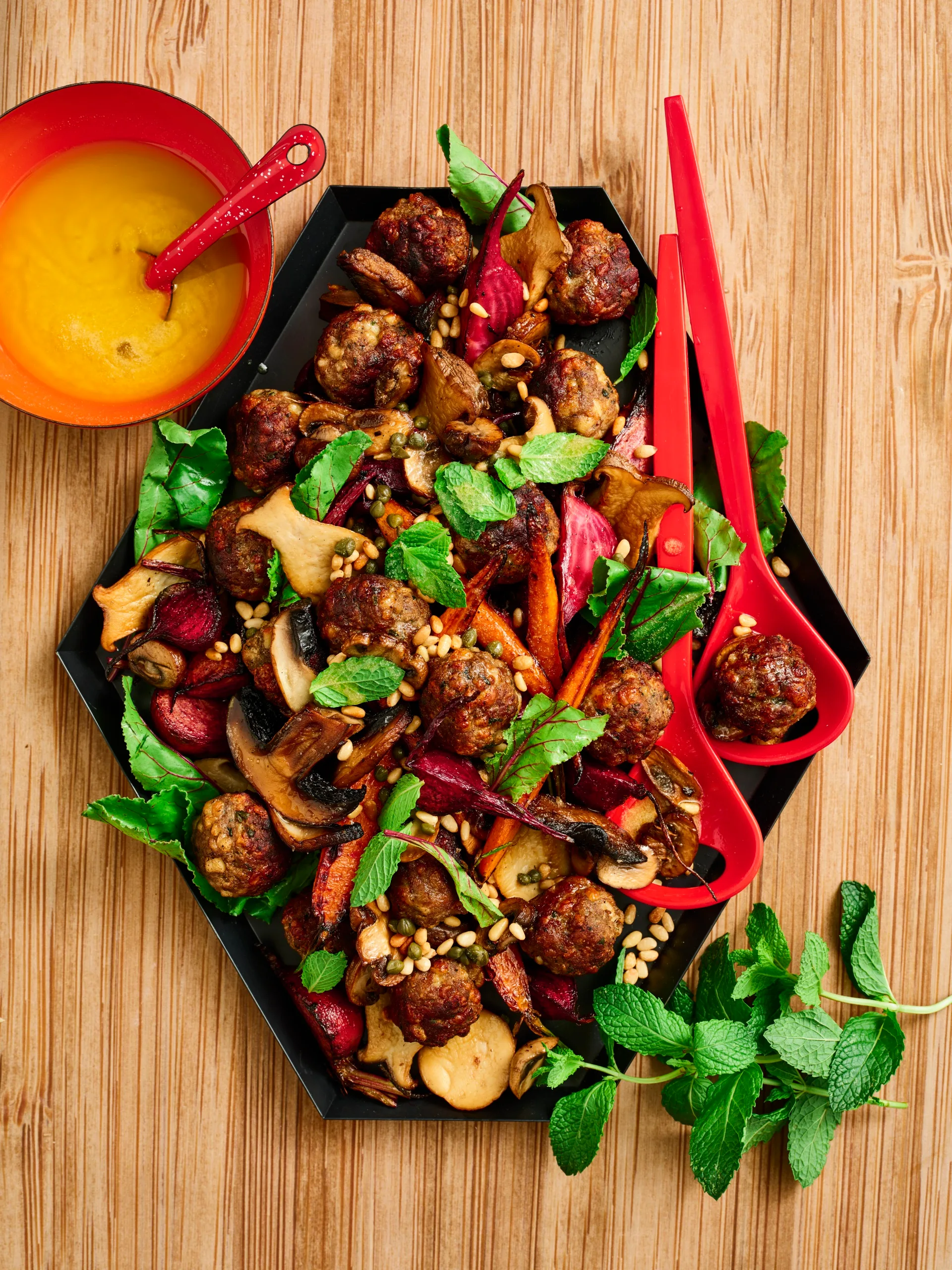 lamb meatballs and autumn vegetables on a hexagonal plate with fresh herbs on top and two red spoons