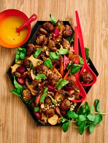 lamb meatballs and autumn vegetables on a hexagonal plate with fresh herbs on top and two red spoons