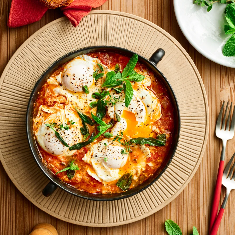 lamb shakshuka with eggs cooked in tomato sauce with fresh herbs on top of bowl