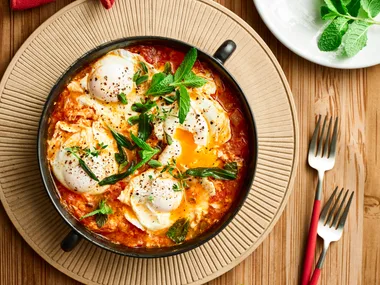 lamb shakshuka with eggs cooked in tomato sauce with fresh herbs on top of bowl