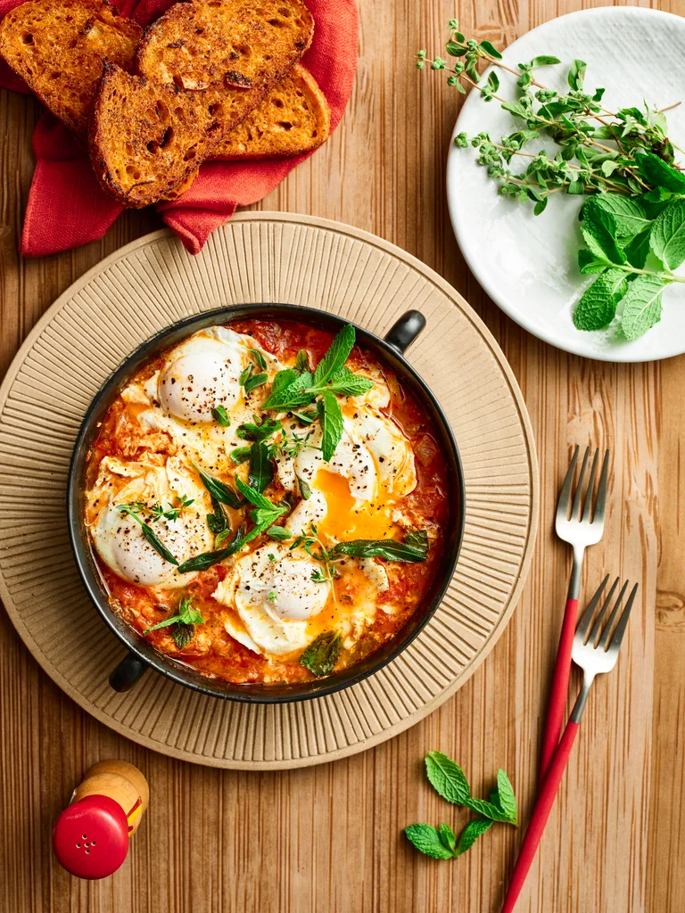 lamb shakshuka with eggs cooked in tomato sauce with fresh herbs on top of bowl