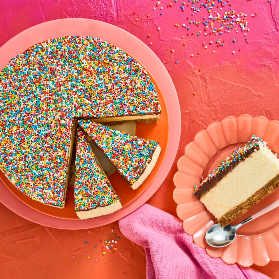 no bake freckly cheesecake on pink plate with several slices cut into it. one slice appears on the right on a peach fluted plate, background is pink to orange ombre