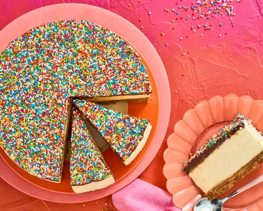 no bake freckly cheesecake on pink plate with several slices cut into it. one slice appears on the right on a peach fluted plate, background is pink to orange ombre