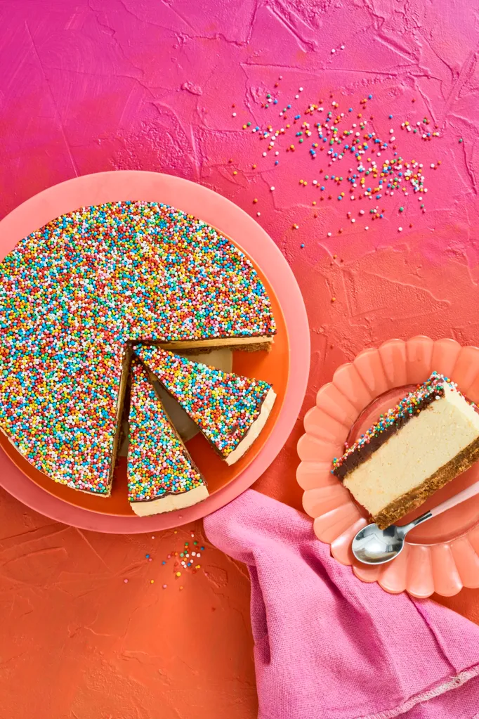 no bake freckly cheesecake on pink plate with several slices cut into it. one slice appears on the right on a peach fluted plate, background is pink to orange ombre